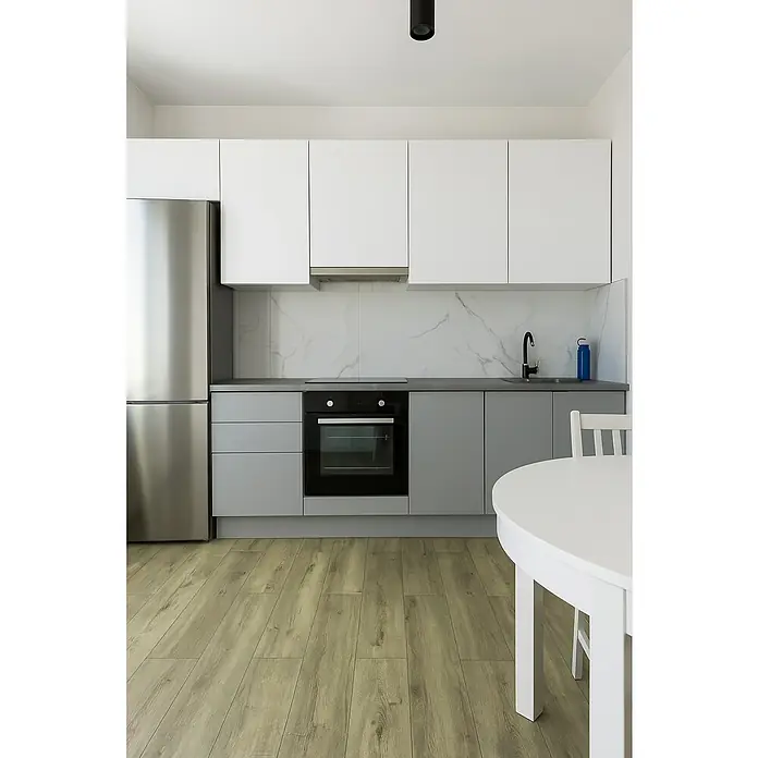 LOGOCLIC Aquaprotect Laminado Roble Mushroom Apollo - 1.288 x 195 x 8 mm, Roble Mushroom Apollo, AC5, Resistente al agua - Vista de la cocina con nevera de acero inoxidable, armarios superiores blancos, inferiores grises y suelos de madera marrón claro.