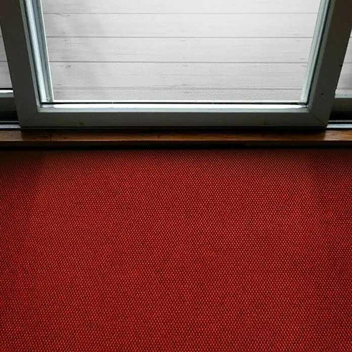 Schmutzfangmatte Hong Kong - Rot, 1.100 x 200 cm, 100 % Polypropylen - Detailaufnahme einer roten Stofffläche unterhalb eines Fensters, das Tageslicht auf eine helle Holzfläche wirft.