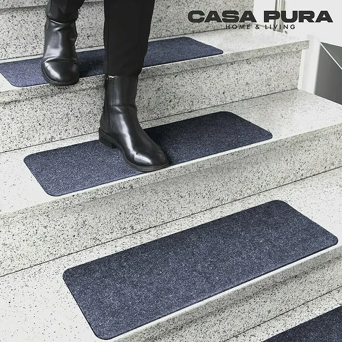 Stufenmatte Leipzig - 60 x 25 cm, 100 % Polypropylen, Blau - Treppenläufer von CASA PURA in Dunkelblau auf einer Treppe mit Person, die die Treppe hochgeht. Die Läufer erhöhen die Sicherheit.