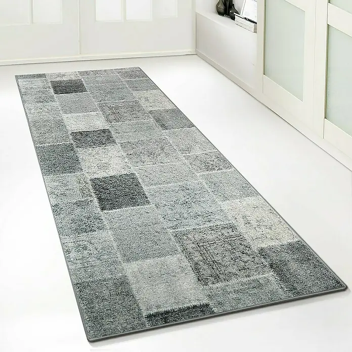 Teppichläufer Monsano - Anthrazit, 250 x 80 cm, 100 % Polyamid - Ein stilvoller, grauer Teppich mit quadratischem Muster liegt auf einem hellen Boden und verleiht dem Raum eine moderne Note.