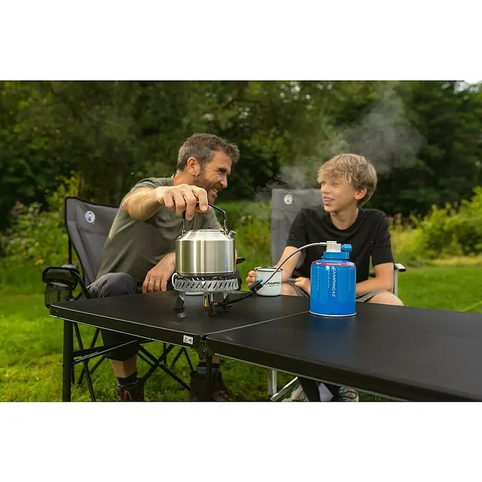 Campingaz Campingkocher Camp & Trek Connect CV - Anzahl Brenner: 1 Stk., 2 kW - Vater und Sohn beim Campen, mit einem Campingtisch, einem Gaskocher und einem silbernen Wasserkessel, aus dem Dampf aufsteigt.