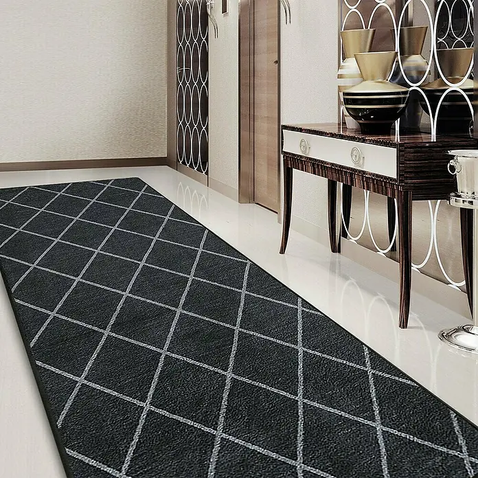 Teppichläufer Cosenza - Schwarz, 450 x 80 cm, 100 % Polyamid - Ein dunkler Teppich mit hellem Rautenmuster liegt in einem Flur. Er ergänzt die Einrichtung mit edlen Möbeln und Vasen.