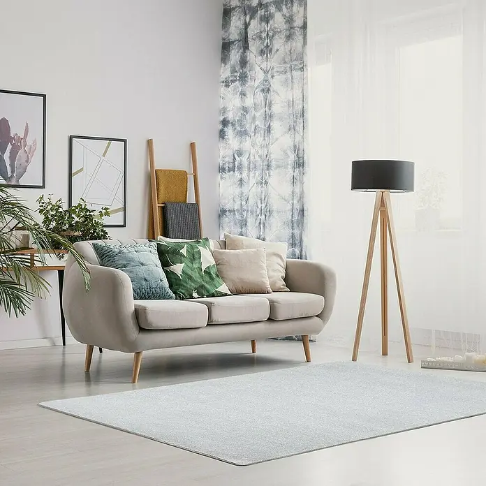 Kurzflorteppich Sundae - Silber, 200 x 200 cm, 100 % Polypropylen - Ein hellgrauer Teppich liegt im Wohnzimmer vor einem Sofa, neben dem ein hölzerner Stehlampe steht. Dekorative Kissen und Pflanzen verschönern den Raum.