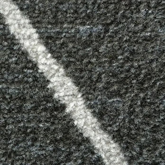 Teppichläufer Cosenza - Schwarz, 450 x 80 cm, 100 % Polyamid - Nahaufnahme eines Teppichs mit diagonalem, weißem Streifen auf grauem Grund. Textur und Farbkontraste des Teppichmusters sind sichtbar.
