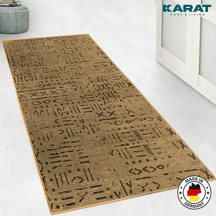 Teppichläufer Vena - Beige, 100 x 80 cm, 65 % Baumwolle, 35 % Polyester - Ein rechteckiger, goldfarbener Teppich mit dunklen Mustern liegt auf einem hellen Boden, mit Hinweisen auf Qualität und Herkunft.