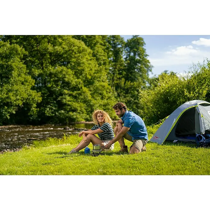 Campingaz Campingkocher Camp & Trek Connect CV - Anzahl Brenner: 1 Stk., 2 kW - Ein Paar bereitet mit einem Coleman Kocher eine Mahlzeit auf einem Campingausflug neben einem Coleman Zelt zu.