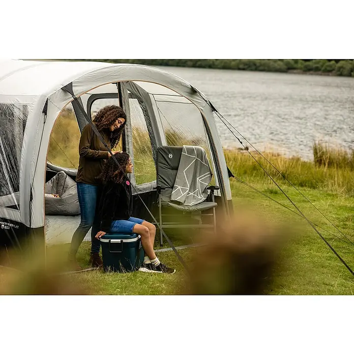 Coleman Kühlbox 52QT Xtreme™ - L x B x H: 56 x 42 x 47 cm, Blau, 49 l - Zwei Frauen vor einem Coleman-Zelt. Eine Frau sitzt auf einer Kühlbox, während die andere ihr Haar richtet. Im Hintergrund befindet sich ein See.