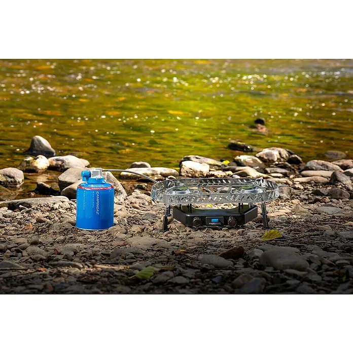 Campingaz Campingkocher Camp & Trek Twin Connect CV - Anzahl Brenner: 2 Stk., 2 kW - Campingkocher und Gaskartusche von Campingaz vor einem Fluss.