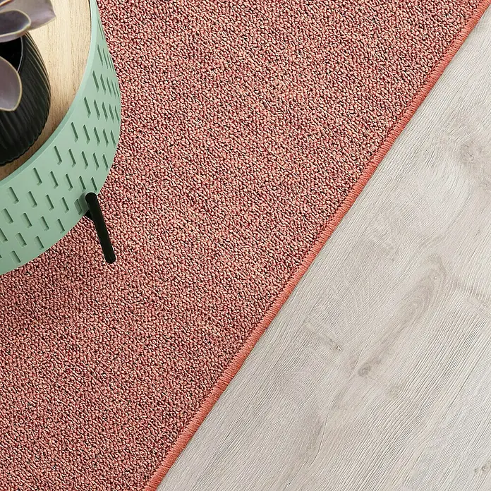 Flachgewebeteppich London - Terra, 200 x 200 cm, 100 % Polypropylen - Nahaufnahme eines rosa Teppichs, der neben einem modernen Beistelltisch auf einem hellen Holzboden liegt.