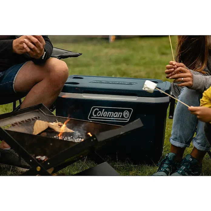 Coleman Kühlbox 52QT Xtreme™ - L x B x H: 56 x 42 x 47 cm, Blau, 49 l - Nahaufnahme eines Coleman Kühlers neben einem Lagerfeuer, während Menschen Marshmallows rösten.