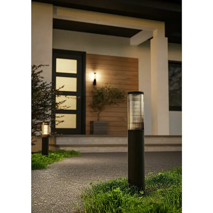 Eglo Lámpara de pie para exterior Salle - 15 W, Color del marco: Negro, Sin bombillas - Una vista exterior de una casa moderna, con luces de bolardo negras que iluminan un camino, creando un ambiente elegante y acogedor.