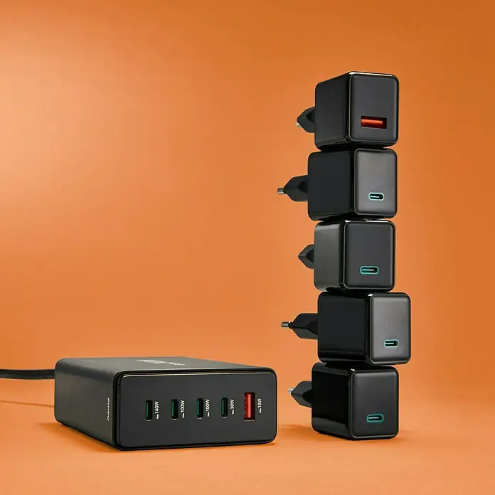 Hama Ladestation 00201977 4 x USB-C, 1 x USB-A - Schwarz - Das Bild zeigt ein Hama Mehrfach-Ladegerät und gestapelte einzelne Ladegeräte auf einem orangefarbenen Hintergrund, die die Ladekapazität betonen.