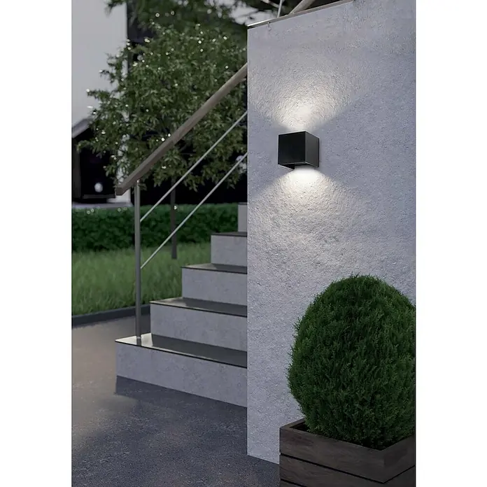 Eglo Aplique exterior LED Barcarola-E - 4,5 W, 10,5 x 10,5 x 10 cm, Negro, IP44, Blanco neutro - La moderna lámpara de pared negra emite luz cálida, iluminando con estilo el área exterior junto a escaleras y un arbusto decorativo.