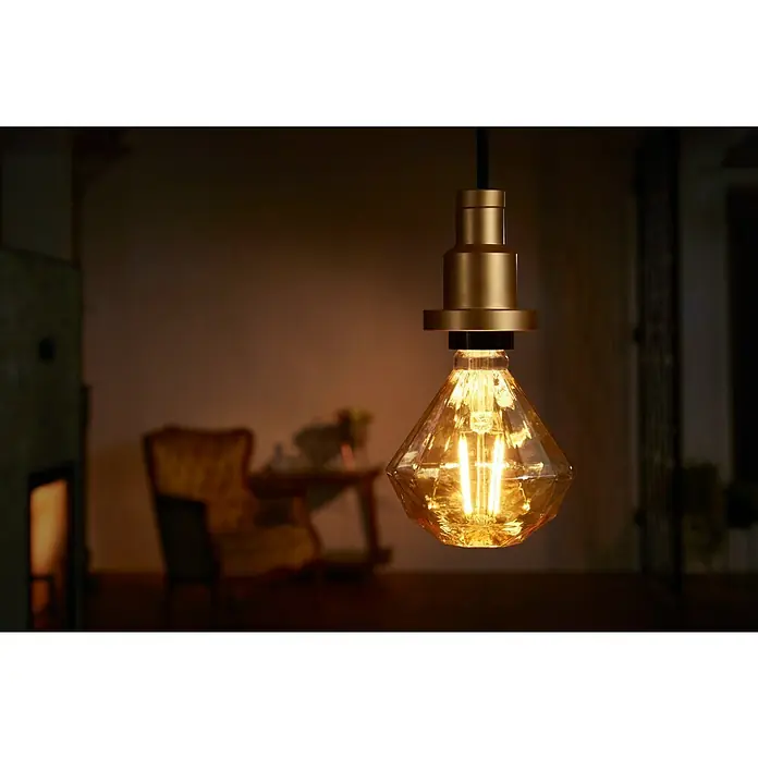 Osram Portalámparas de cuerda Vintage 1906 Pendulum Gold - Oro, 200 cm, 60 W, E27 - Primer plano de una bombilla en forma de diamante con accesorios dorados, que emite un brillo cálido y acogedor en un espacio elegante.