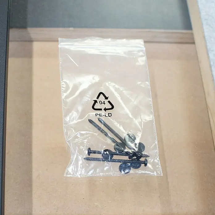 Inova Aluminiumfenster Loft Innenfenster Glas -  - Nahaufnahme einer durchsichtigen Plastiktüte mit schwarzen Schrauben und Unterlegscheiben darin, die auf einer Holzoberfläche liegt.