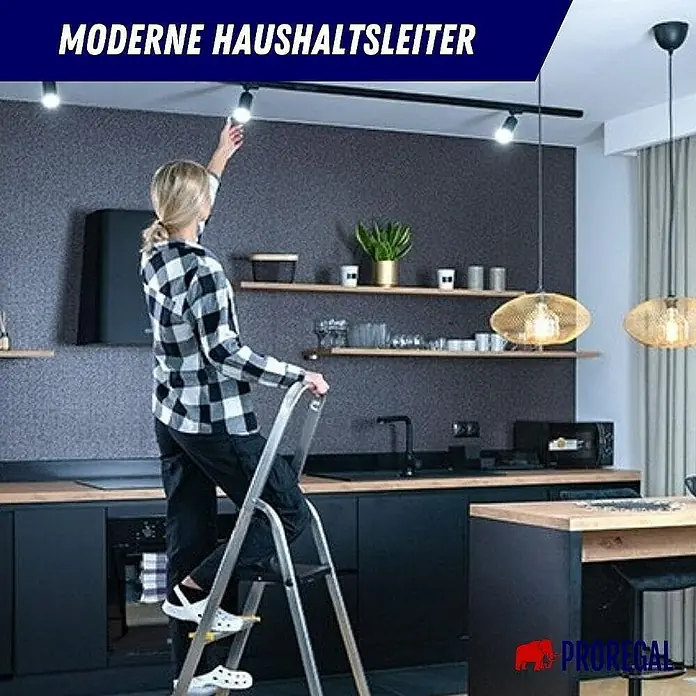 Proregal Stehleiter ATLAS mit Werkzeugablage & Handlauf - Anzahl Tritte: 6 Stk., Arbeitshöhe: 3.190 mm, Belastbarkeit: 150 kg, Aluminium - Eine Frau wechselt eine Glühbirne auf einer modernen Haushaltsleiter in einer stilvollen Küche. Praktisch & sicher für den Haushalt.
