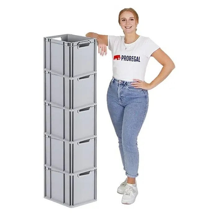 Proregal Euroboxen-Set 5x Eurobox NextGen Grip - Kunststoff, Grau, 5 Stk. - Frau posiert neben einem Stapel grauer Lagerboxen von Proregal. Die robusten Kunststoffboxen sind ideal für Lagerung und Organisation.