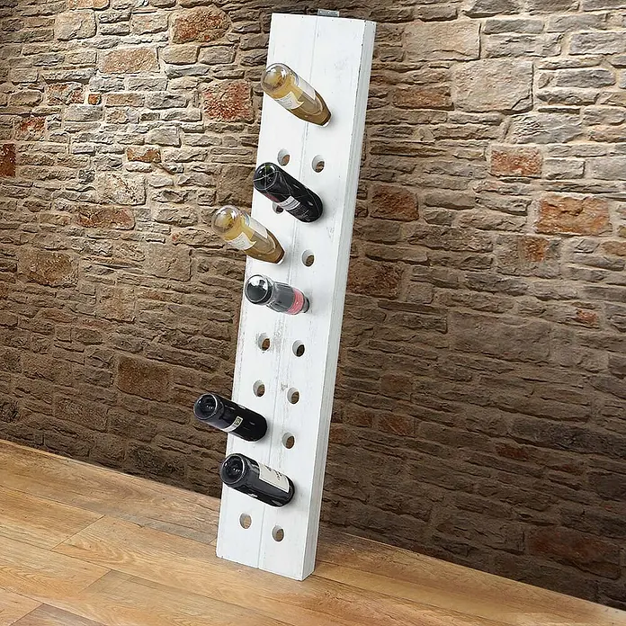 Berlinlodge Flaschenregal Rüttelbrett Weinregal für 20 Flaschen - Holz - Ein weißes Weinregal aus Holz lehnt an einer Ziegelwand und bietet Platz für mehrere Weinflaschen.