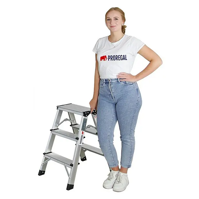 Proregal Doppel-Klapptritt APOLLO - Anzahl Tritte: 6 Stk., Arbeitshöhe: 2.000 mm, Belastbarkeit: 150 kg, Aluminium - Frau posiert neben einer Proregal-Trittleiter. Die Trittleiter bietet mit ihren Stufen sicheren Stand für Arbeiten in der Höhe.