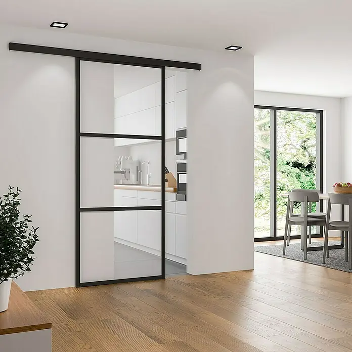 Inova Schiebetür-Komplettset Glasschiebetür ESG Klarglas 1025 x 2200 mm mit Softclose - 1.025 x 2.200 mm - Modernes Interieur mit einer eleganten Glasschiebetür mit schwarzem Rahmen, die den Raum optisch trennt und gleichzeitig Helligkeit bewahrt.
