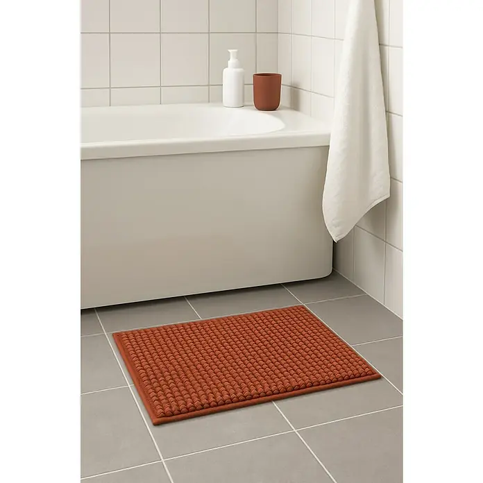 MSV Alfombra de baño Chenille - 60 x 40 cm, Poliéster, Terracota - Una alfombra de baño rectangular, marrón rojizo con textura nudosa, se encuentra frente a una bañera sobre baldosas gris claro.