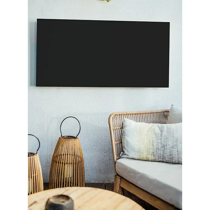 Jokerarea Infrarotheizkörper Area Warm 900 - L x B x H: 120 x 60 x 2,7 cm, 900 W, Schwarz - Elegante Szene mit einem schwarzen Bild an einer weißen Wand, begleitet von Laternen und einem gemütlichen Sessel mit Kissen.