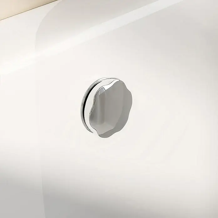Home Deluxe Eckbadewanne ELARA - Weiß - Nahaufnahme eines glänzenden, silberfarbenen Badewannenabfluss-Drehknopfes auf einer weißen Oberfläche.