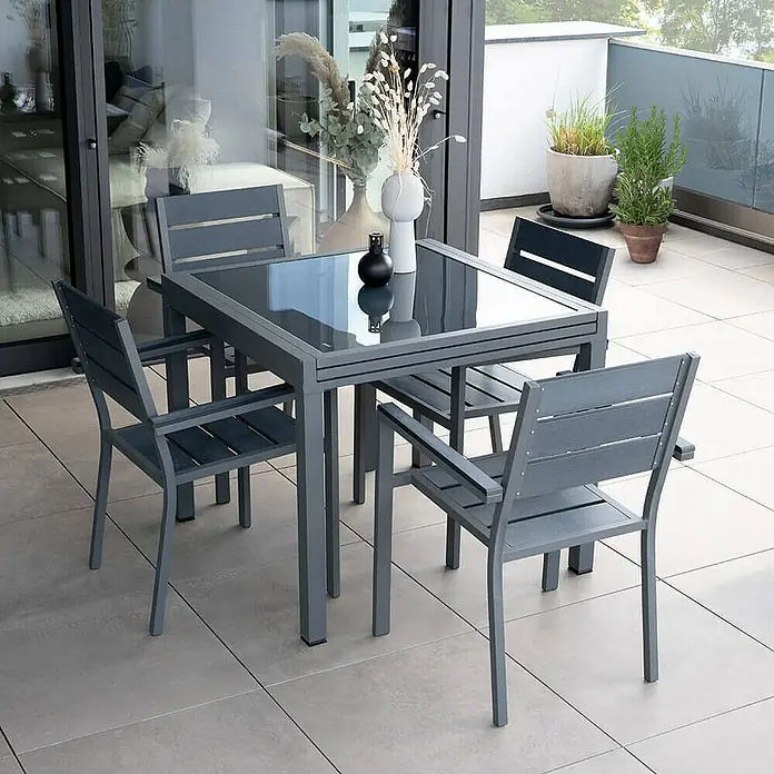 Home Deluxe Gartentisch-Set VERANO MADERA - Tisch inkl. 4 Stühlen - Gesamtumfang: 5 -tlg., Ausziehbar - Grauer Gartentisch mit vier Stühlen auf einer Terrasse. Das Set hat eine Glasplatte und ein modernes Design.