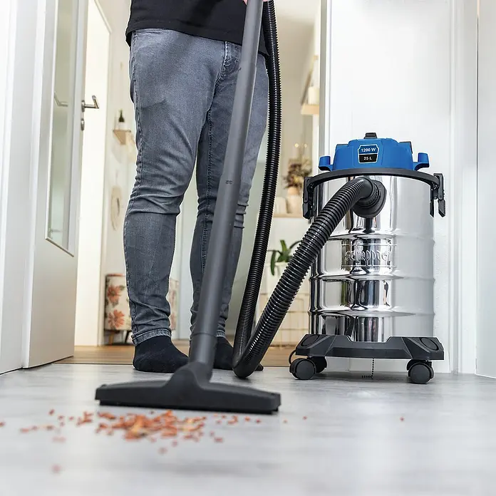 Scheppach Elektro-Nass- & Trockensauger VC25 - Behältervolumen: 25 l, Manuell - Staubsauger bei der Reinigung von Schmutz auf dem Boden, Modell mit Chrombehälter und blauem Oberteil.