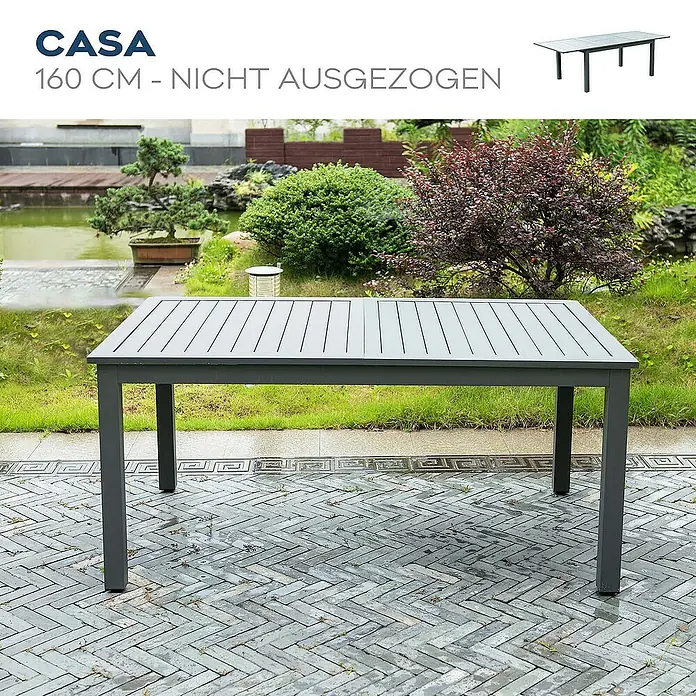 Home Deluxe Gartentisch-Set CASA MADERA - Tisch inkl. 4 Stühlen - Gesamtumfang: 5 -tlg., Ausziehbar - Grauer CASA Gartentisch, 160 cm lang, nicht ausgezogen, auf gepflasterter Terrasse mit Garten im Hintergrund.
