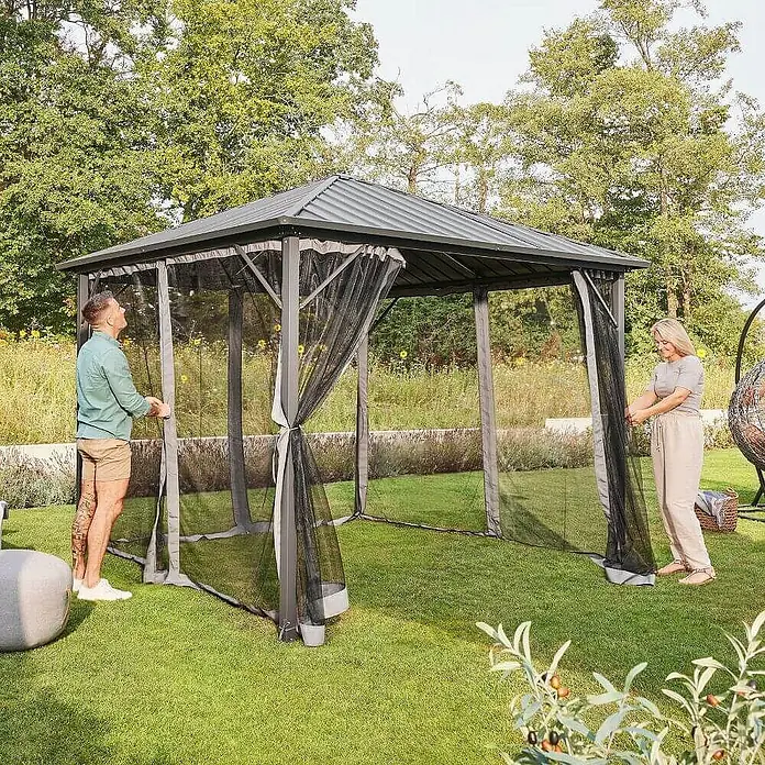 Home Deluxe Standard-Pavillon AZUR - B x T: 298 x 298 cm, Farbe Gestell: Anthrazit, Metall - Ein Paar steht vor einem stilvollen Pavillon mit Moskitonetzen im Garten. Der Pavillon bietet Schutz und Eleganz für Outdoor-Aktivitäten.