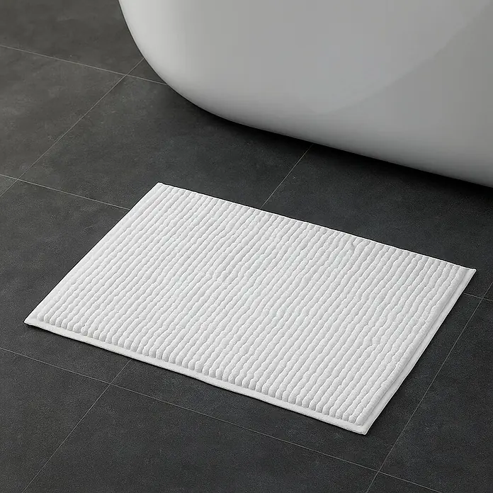 MSV Alfombra de baño Chenille - 60 x 40 cm, Poliéster, Blanco - Una alfombra de baño rectangular blanca con un patrón de rayas se encuentra sobre baldosas grises junto a una bañera blanca.