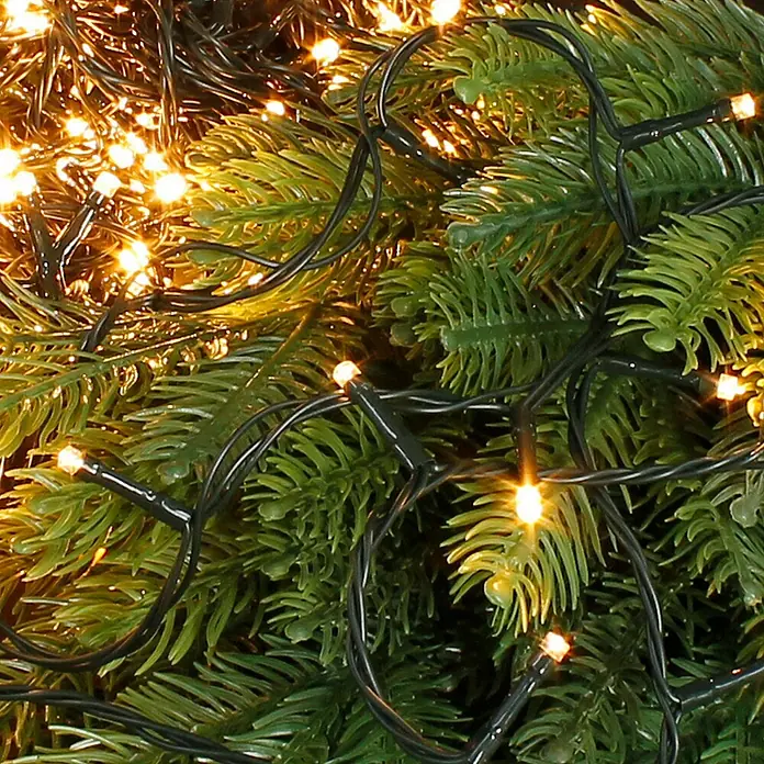 ECD Germany LED-Lichterkette - Außen, Lichtfarbe: Warmweiß, Anzahl Leuchtmittel: 320 Stk., Netzbetrieben - Nahaufnahme einer Lichterkette mit warmweißem Licht, gewunden um einen grünen Weihnachtbaum, die eine festliche und gemütliche Atmosphäre schafft.