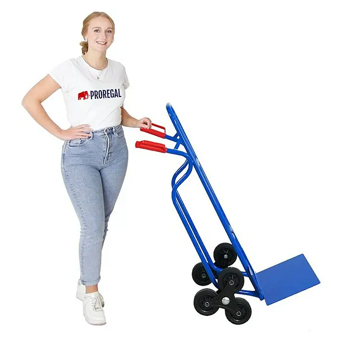 Proregal Treppen-Sackkarre RAGNAR mit klappbarer XXL Schaufel & Vollgummibereifung - Stahl, Traglast: 250 kg - Frau neben einem Treppensteiger-Sackkarre mit sechs Rädern und blauem Rahmen mit roten Griffen.