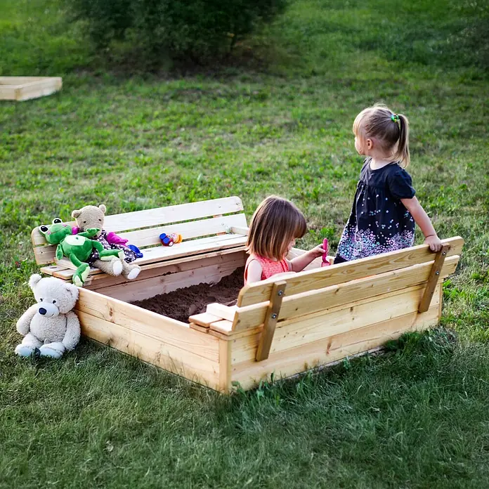 Timbela Sandkasten - L x B: 122 x 118 cm, Holz, Natur - Ein hölzerner Sandkasten mit integrierter Bank und zwei Kindern beim Spielen im Garten. Teddybären und anderes Spielzeug sind ebenfalls zu sehen.