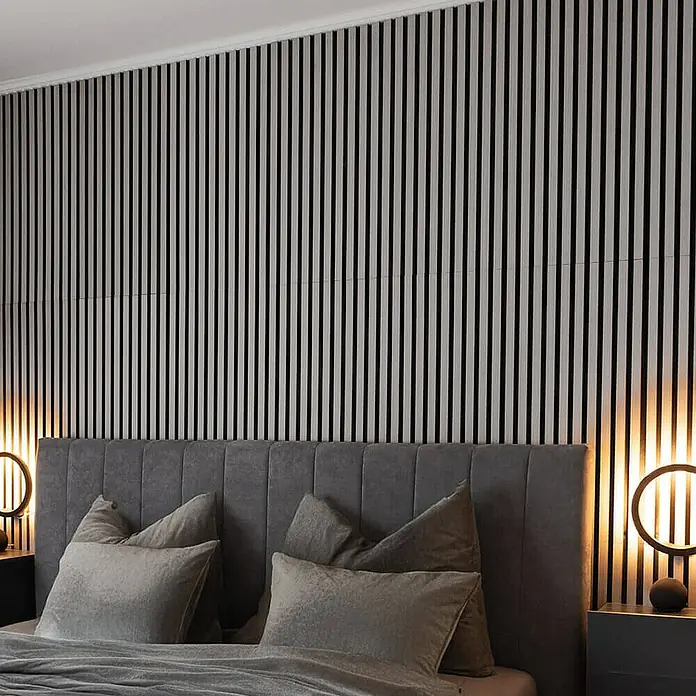 Home Deluxe Akustikpaneel SONIC - Grey Oak 6er Set - Grau, L x B x S: 2,1 cm x 40 cm x 21 mm, 6 Stk., 1,94 m² - Blick auf ein Schlafzimmer mit einem großen Bett mit vielen Kissen und einer Wand mit Holzpaneelen im Hintergrund.