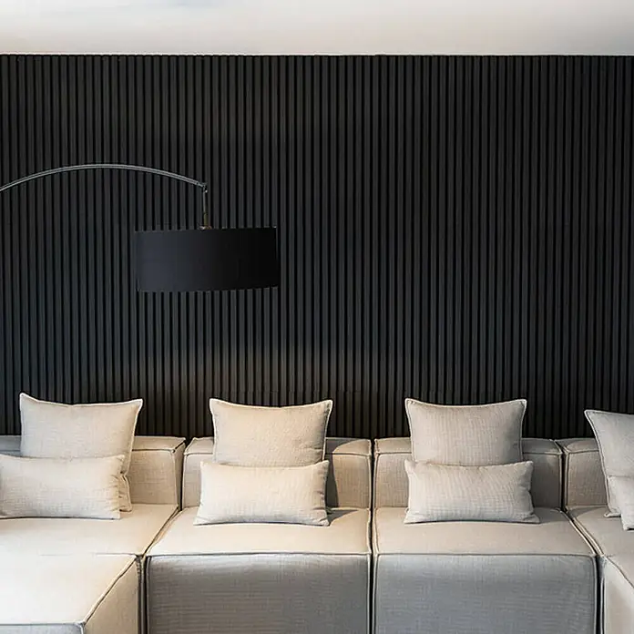 Home Deluxe Akustikpaneel SONIC - Black Oak 12er Set - Schwarz, L x B x S: 2,2 cm x 40,5 cm x 22 mm, 12 Stk., 3,88 m² - Eine moderne Wohnzimmerszene mit modularem Sofa und stilvoller Stehlampe vor einer dunklen Akzentwand. Das modulare Sofa bietet Komfort und Stil.