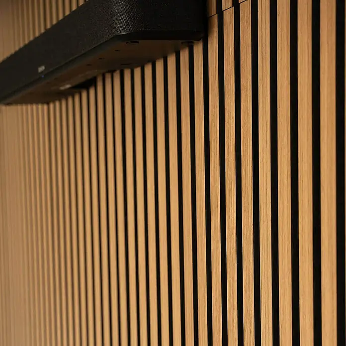 Home Deluxe Akustikpaneel SONIC - Oiled Oak 6er Set - Eiche, L x B x S: 2,2 cm x 40,5 cm x 22 mm, 6 Stk., 1,94 m² - Detailaufnahme einer schwarzen Soundbar an einer Wand mit Holzlattenverkleidung.