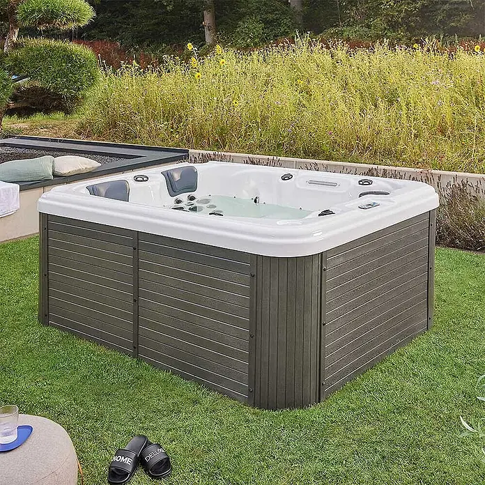 HOME DELUXE Outdoor Whirlpool BEACH Pure -  - Ein luxuriöser Whirlpool mit grauem Gehäuse und weißem Rand steht im Garten.