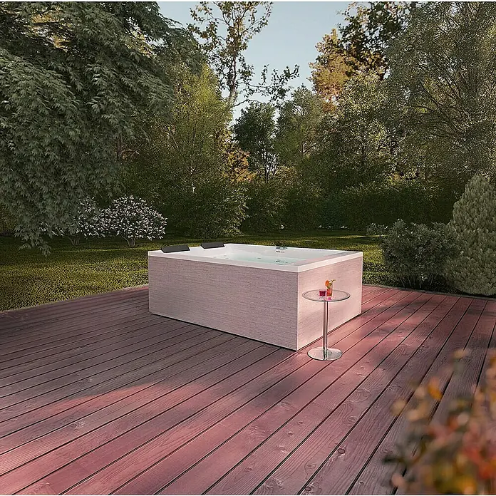 Home Deluxe Außen-Whirlpool NIMBUS PURE - Weiß, Max. Personenzahl: 2 Stk. - Ein moderner Whirlpool mit stilvoller Holzverkleidung auf einer Terrasse, umgeben von üppigem Grün. Perfekt zum Entspannen im Freien.
