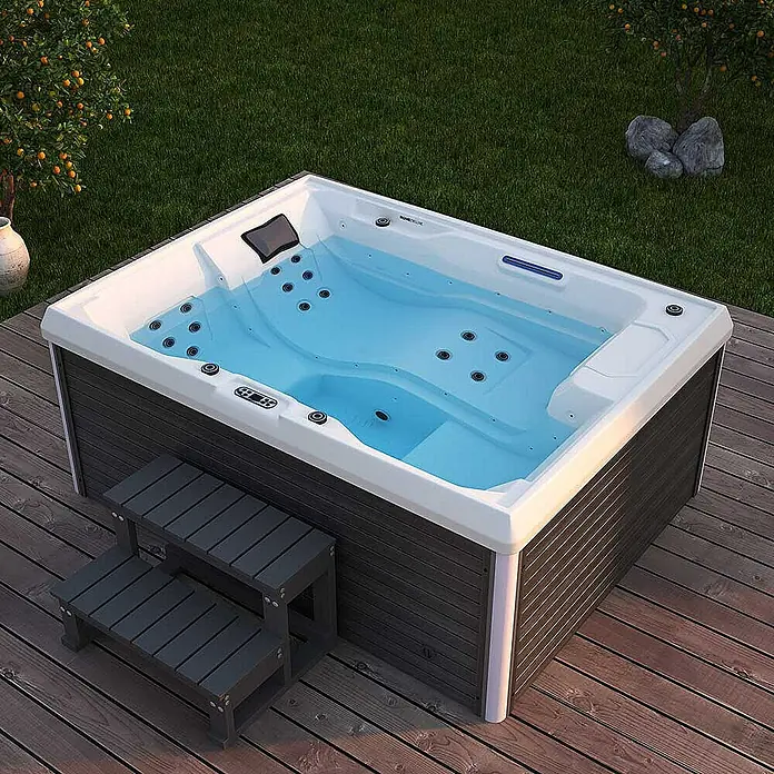 Home Deluxe Außen-Whirlpool STREAM inkl. Treppe und Thermoabdeckung - Anthrazit, Max. Personenzahl: 3 Stk. - Elegantes, rechteckiges Outdoor-Whirlpool mit integrierter Treppe auf einer Holzterrasse, umgeben von Grün.