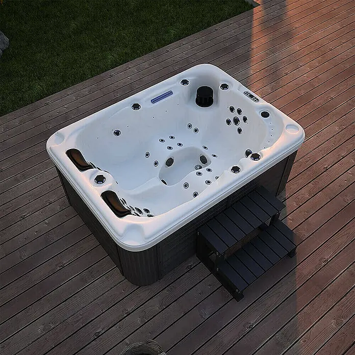 Home Deluxe Outdoor Whirlpool BEACH Mit Treppe und Thermoabdeckung -  - Ein luxuriöser Whirlpool mit Einstiegstreppe auf einer Holzterrasse, umgeben von Grün. Entspannung pur im eigenen Garten.