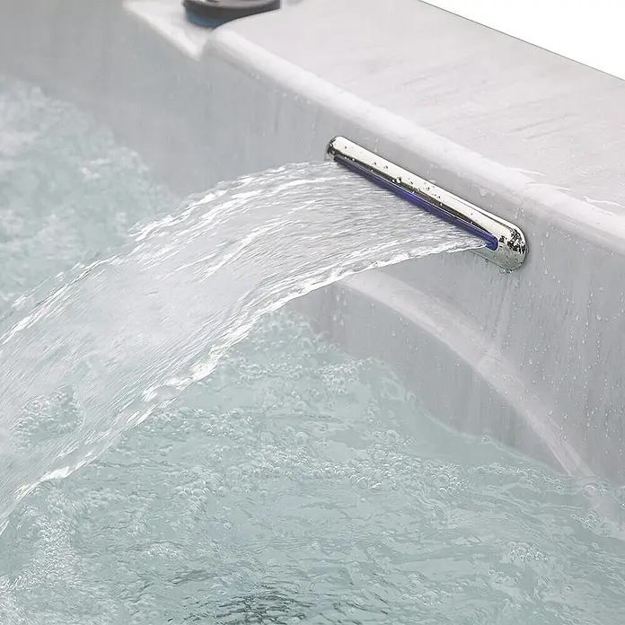 HOME DELUXE - Outdoor Whirlpool WHITE MARBLE PURE - 210 x 160 cm für 3 Personen | Ausstattung: Pure -  - Nahaufnahme eines Whirlpools mit einem modernen Wasserfall, der mit blauen LEDs beleuchtet ist.