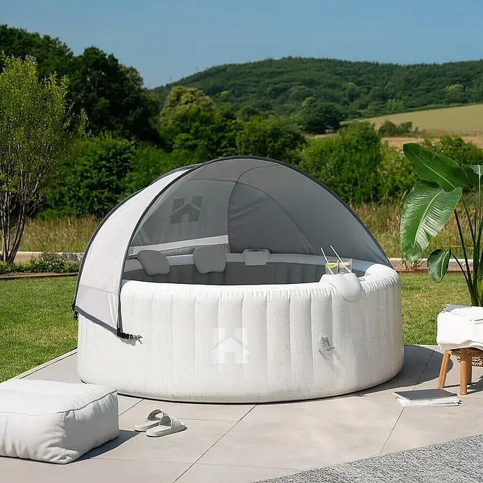 Home Deluxe Außen-Whirlpool SPLASH inkl. Kissen, Getränkehalter und Sonnendach - 208 x 208 x 65 cm, Beton, Max. Personenzahl: 6 Stk. - Bild eines aufblasbaren Whirlpools mit Überdachung auf einer Terrasse. Der Whirlpool ist von Grünflächen umgeben.