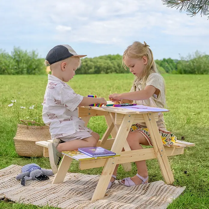 Timbela Kinder-Picknicktisch - 81 x 60 x 50 cm, Holz, Ohne Staufach - Zwei Kinder sitzen an einem hölzernen Picknicktisch im Freien und malen. Der Tisch ist aus hellem Holz gefertigt und bietet eine tolle Malfläche.