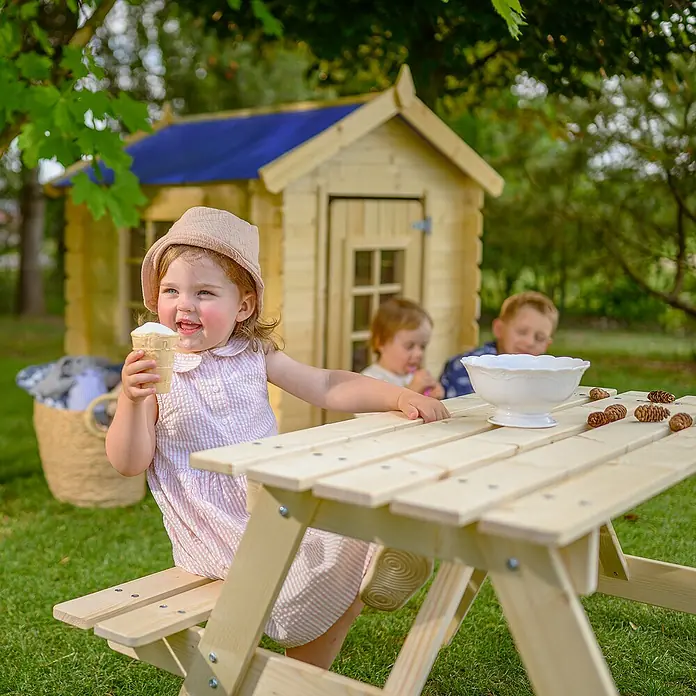 Timbela Kinder-Sitzgruppen-Set - 90 x 90 x 50 cm, Holz, Ohne Staufach - Ein Kind genießt ein Eis am Picknicktisch aus Holz im Garten, während andere Kinder im Hintergrund spielen.