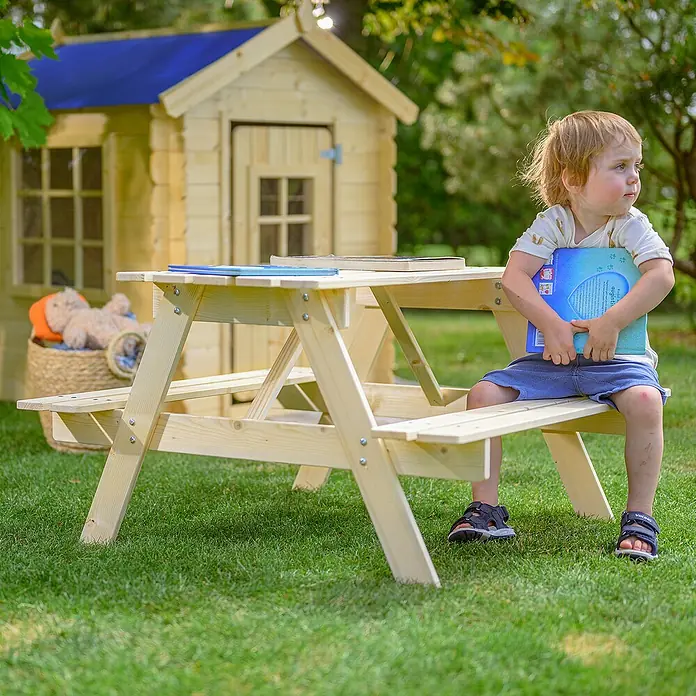 Timbela Kinder-Sitzgruppen-Set - 90 x 90 x 50 cm, Holz, Ohne Staufach - Ein Kind sitzt an einem hellen Holz-Picknicktisch für Kinder im Garten, im Hintergrund ein Spielhaus.