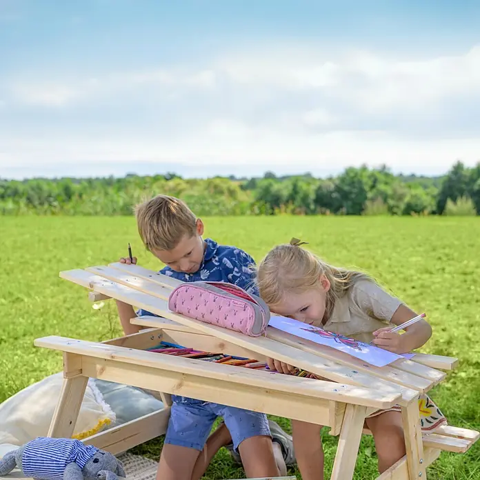 Timbela Kinder-Sitzgruppen-Set - 90 x 90 x 50 cm, Holz, Mit Staufach - Ein Holztisch mit zwei Kindern, die darauf malen, Stifte, ein Mäppchen und ein Kuscheltier sind auch dabei.