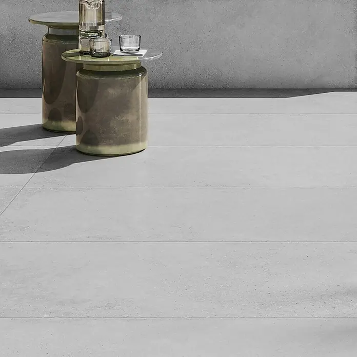 Terrassenfliese Moonstone White - 60 x 120 x 2 cm, Weiß, Matt - Elegante Keramiktische mit Getränken auf einem stilvollen, grauen Fliesenboden. Das minimalistische Design und die sanften Farben schaffen eine ruhige Atmosphäre.