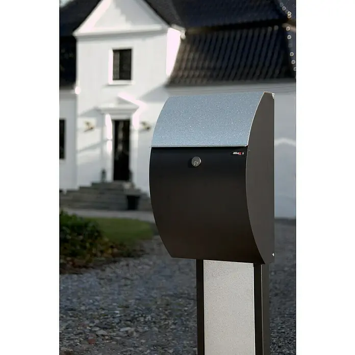 Allux Briefkasten 7000 - L x B x H: 195 x 320 x 510 mm, Schwarz / Silber, Stahl - Nahaufnahme eines modernen Allux Briefkastens mit silbernem Deckel und schwarzem Korpus vor einem Haus.